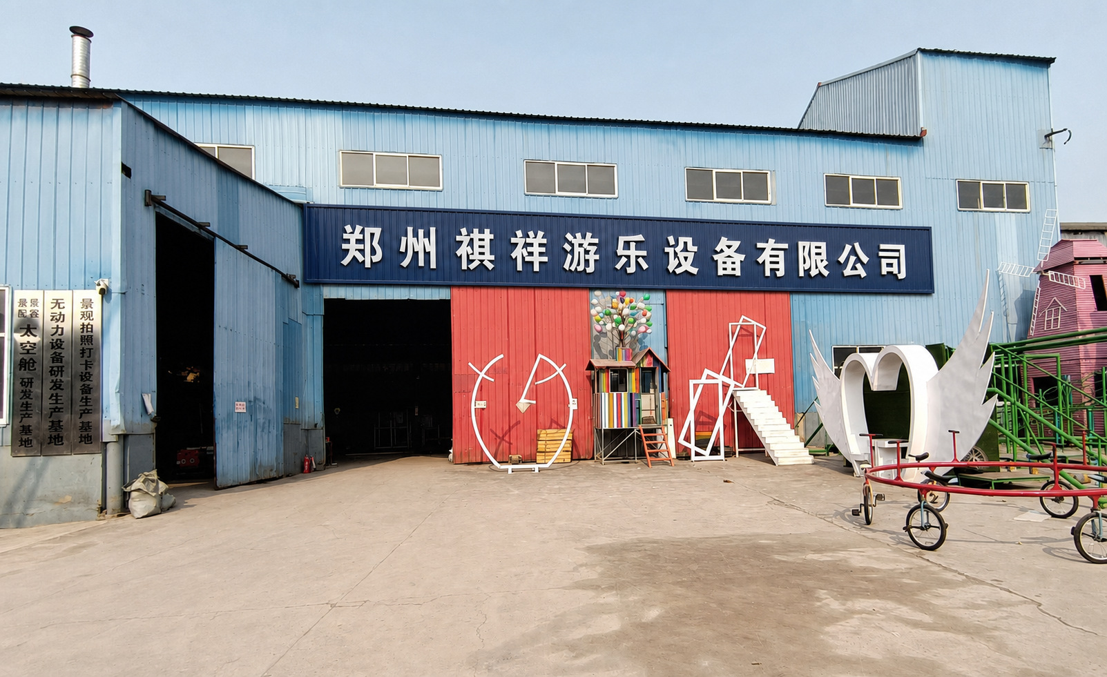 郑州祺祥游乐设备有限公司厂区门口。蓝色牌匾写公司全称，院内摆着打卡装置样品。